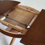 Table ronde vintage à rallonge en chêne massif éditée par Lübke, Allemagne années 60, estampille d'origine sous le plateau, piétement central à quatre jambes plates croisées en X réunies par un moyeu rond, allonge centrale
