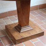 Table ronde vintage en frêne art déco, plateau circulaire à chant arrondi, pied central en colonne carrée sur socle mouluré à degrés, bois traité et rénové