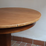 Table ronde vintage en frêne art déco, plateau circulaire à chant arrondi, pied central en colonne carrée sur socle mouluré à degrés, bois traité et rénové