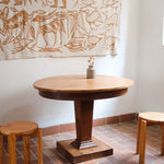 Table ronde vintage en frene art déco, plateau circulaire à chant arrondi, pied central en colonne carrée sur socle mouluré à degrés, bois traité et rénové