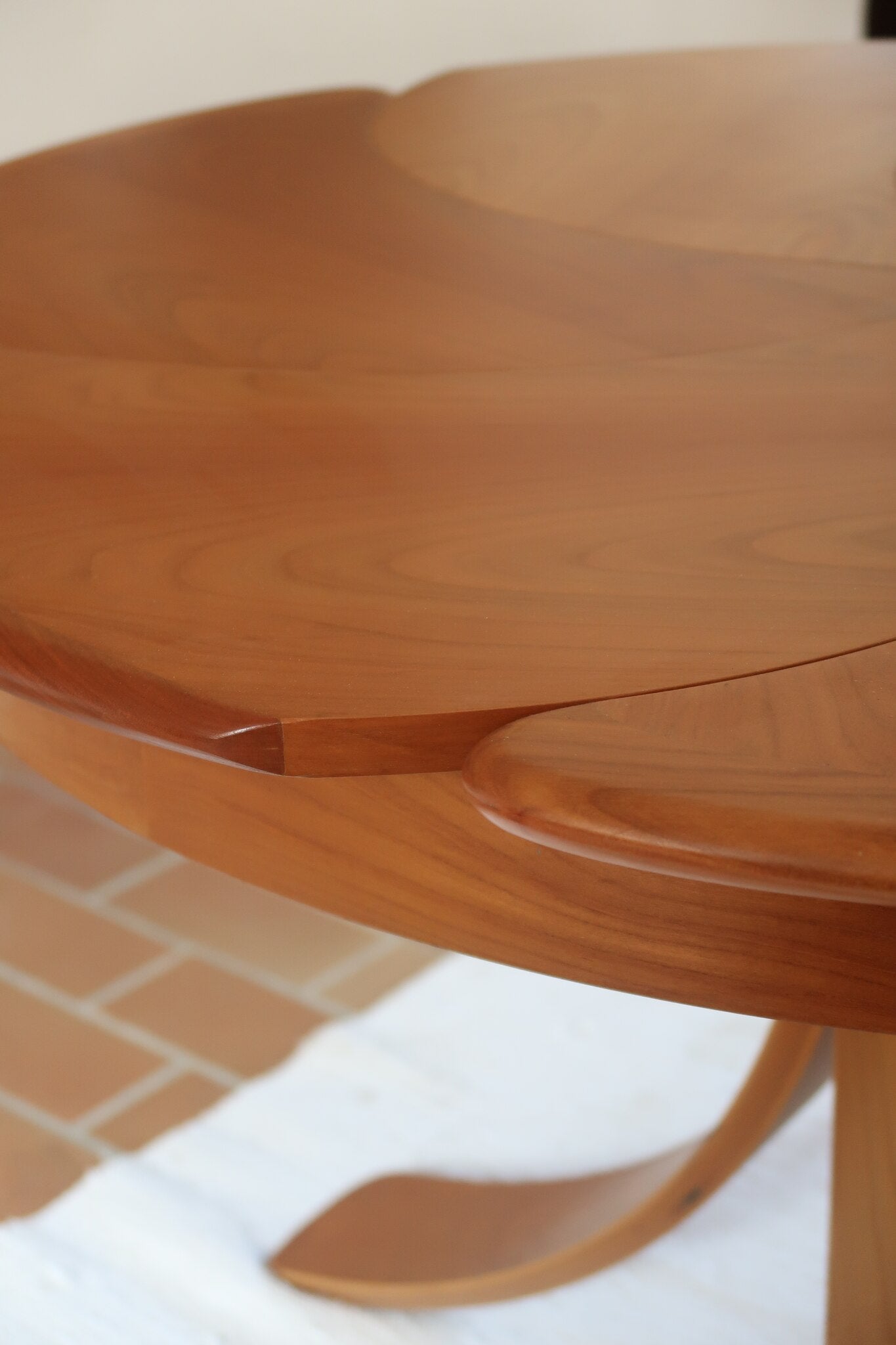 Table ronde vintage en orme massif années 80, prototype jamais produit, plateau fixe composé de six segments dessinés en pétales autour du centre, piétement central à quatre jambes larges cintrées