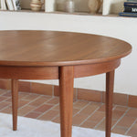 Table à manger ronde extensible vintage en teck miel, pieds fuseau, deux rallonges jusqu'à douze couverts, style scandinave fabrication française années 60