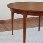 Table à manger ronde extensible vintage en teck miel, pieds fuseau, deux rallonges jusqu'à douze couverts, style scandinave fabrication française années 60