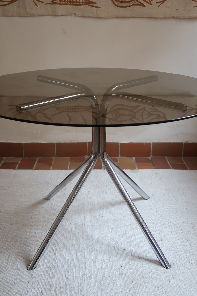 Table ronde années 70 avec plateau en verre fumé et piètement chromé sculptural à quatre branches.