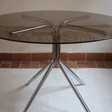 Table ronde années 70 avec plateau en verre fumé et piètement chromé sculptural à quatre branches.