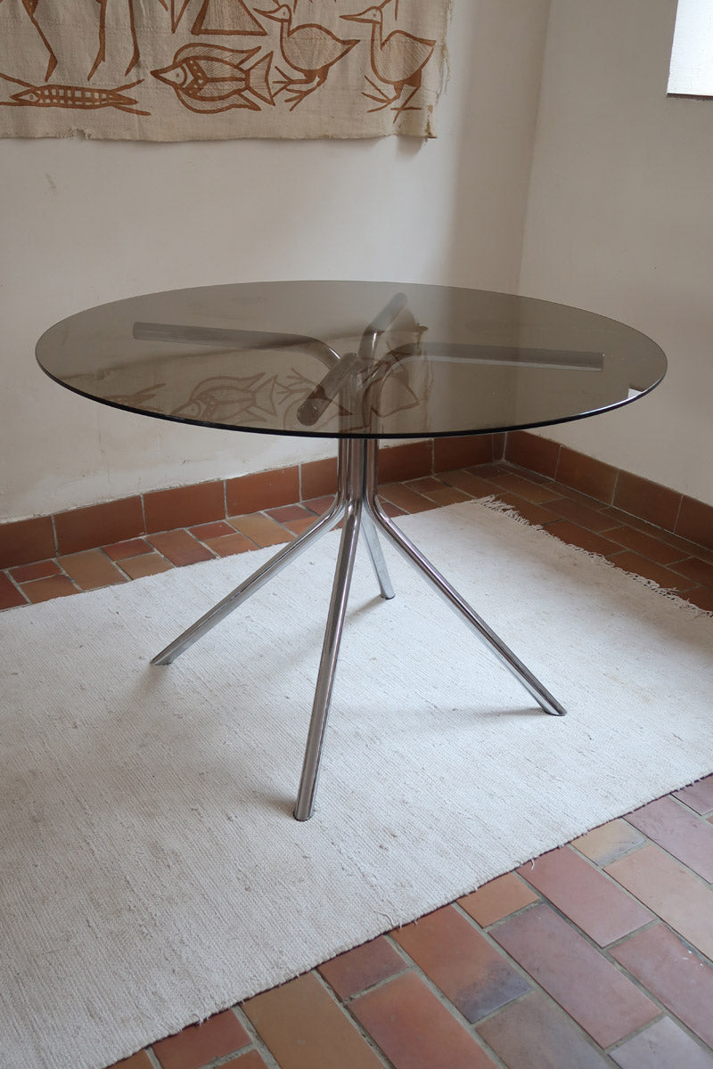 Table ronde années 70 avec plateau en verre fumé et piètement chromé sculptural à quatre branches.