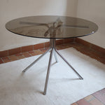 Table ronde années 70 avec plateau en verre fumé et piètement chromé sculptural à quatre branches.